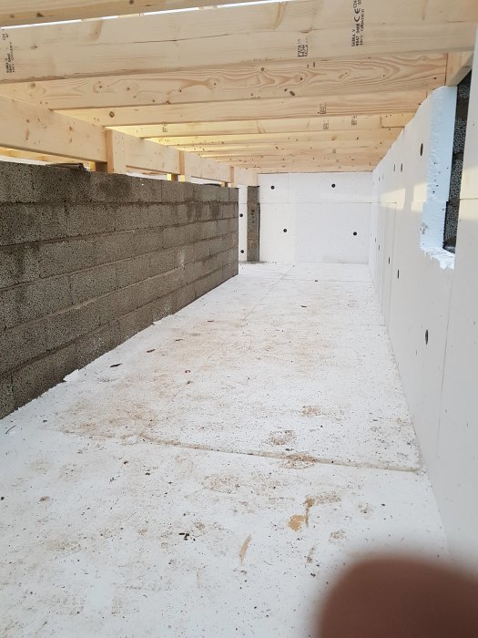 Grund till en byggnad med isolering, betongplatta och staplade betongblock under träbjälklag.