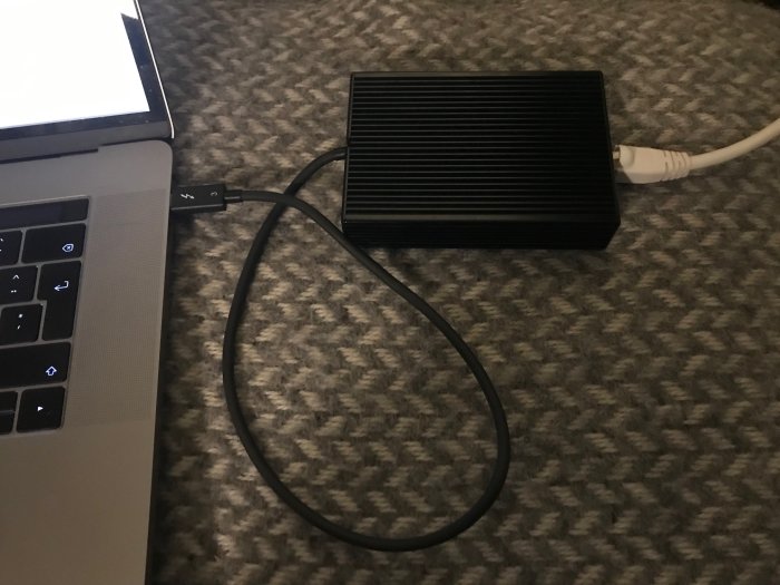 MacBook Pro ansluten till en Ethernet-adapter med en Cat6-kabel på ett grått underlag.