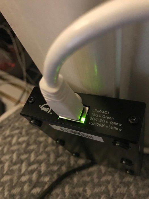 Ethernet-adapter kopplad till en vit nätverkskabel och indikatorljus som visar anslutningshastighet.