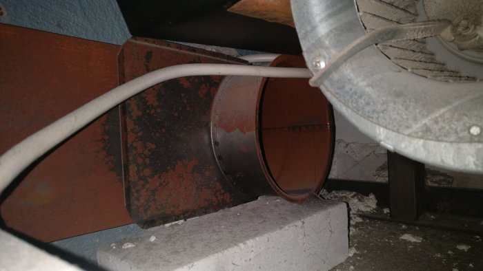 Utsikt genom luftintag visar ett spjäll och spirorör i en braskamininstallation.