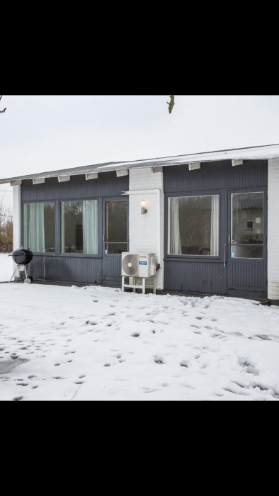 Husfasad med två sektioner av fönster och altandörrar som skal renoveras, vintertid med snö.