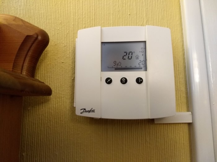 Danfoss ECA61 reglerpanel med inbyggd rumsgivare på en vägg, visar temperatur och menyalternativ.