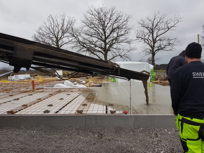 Gjutning av grund med betongbil och arbetare i säkerhetskläder på en byggarbetsplats.