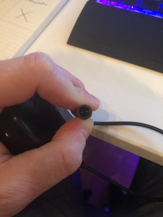 Hand håller en strömadapter till trallbelysning med synlig kontakt och kabel.
