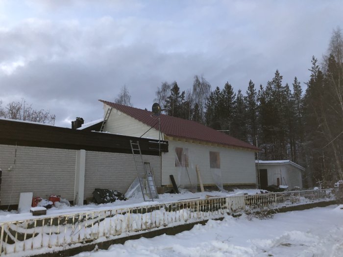 Hus under renovering med isolerade och med plywood igengjutna fönsteröppningar, omgivet av snö.