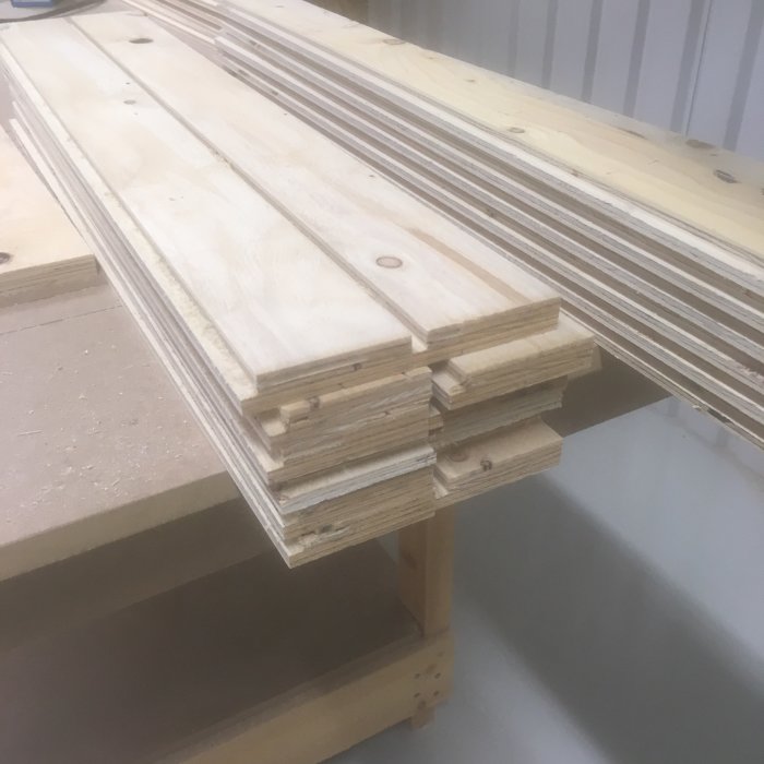 Trälistar med falsade kanter staplade på en verkstadsbänk i ett ljus verkstadsutrymme.