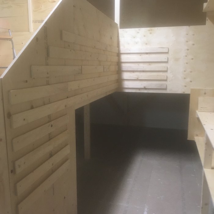 Hörn av en hobbyverkstad med trähyllor och lister för verktygsorganisering genom French cleat-systemet.