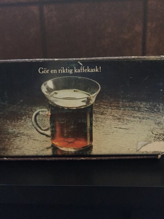 Ett gammalt kaffeglas med en 25-öring i botten, texten "Gör en riktig kaffekask!" ovanför.