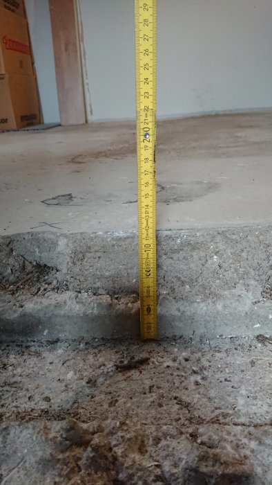 Måttband visar höjdskillnaden mellan betonggolv och grund i ett garage under renovering.