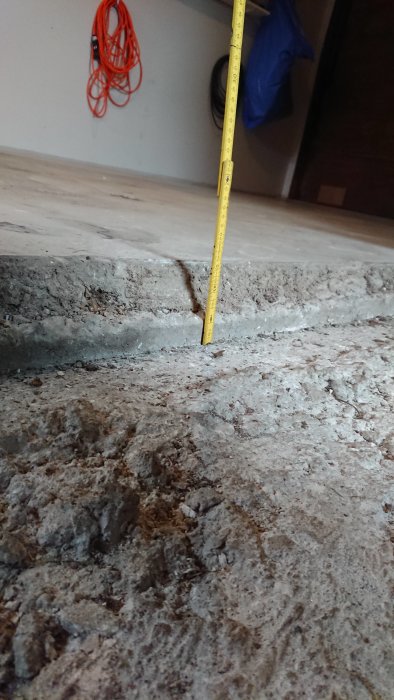 Mätning av höjdskillnad på betonggolv i garage med måttband.