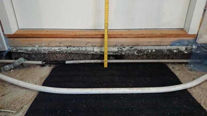 Mätning av garagets väggisoleringstjocklek med tumstock vid golvsockeln.