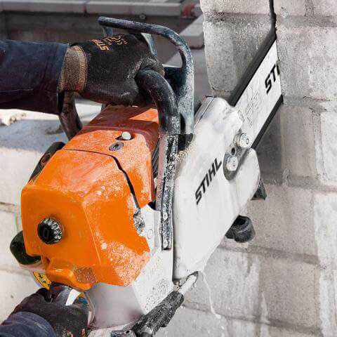 Person som använder en orange och vit STIHL betongsåg för att såga i en betongvägg.