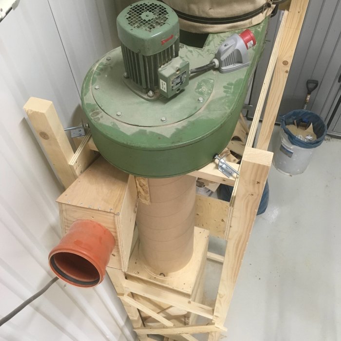 En hemgjord träcyklon för spånhantering monterad på ett träställning, med övergångsdel och fläktenhet.