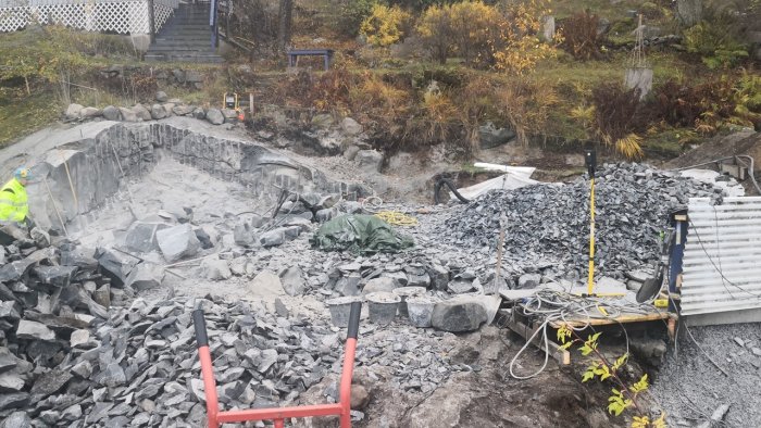 Byggarbetsplats med berggrund och sprängsten, verktyg, och arbetsmaterial synliga.