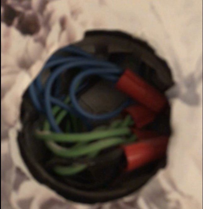 Suddig bild på en öppen elektrisk dosa med gröna och blå kablar samt röda skarvhylsor.