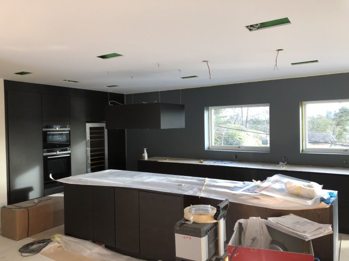 Kök under renovering med upphängd köksfläkt och omonterade bänkskivor.