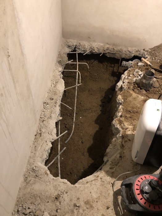 Uppgrävt hål i källargolv med synliga rör och fuktproblem efter dränering.