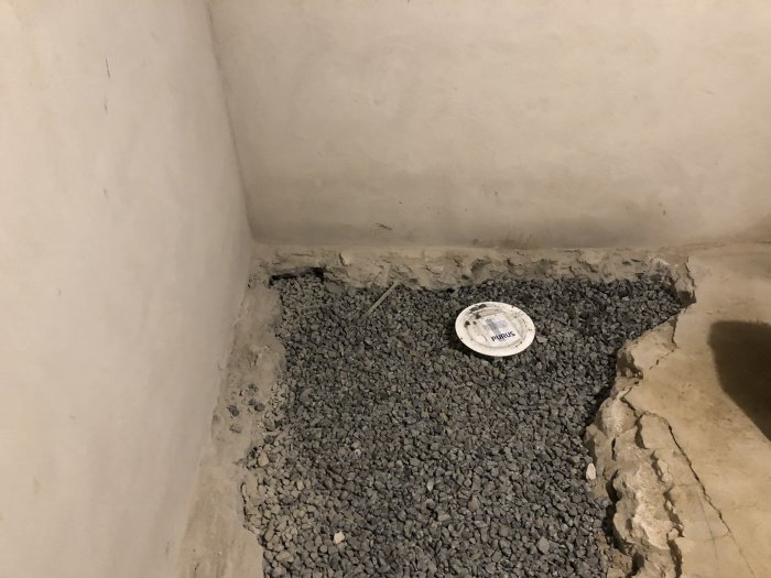 Hörn av en källare med nybilat golv fyllt med singel, dräneringsproblem syns med fukt och vatteninträngning.