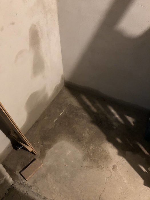 Källarhörn med fuktfläckar på vägg och golv som indikerar vatteninträngning.