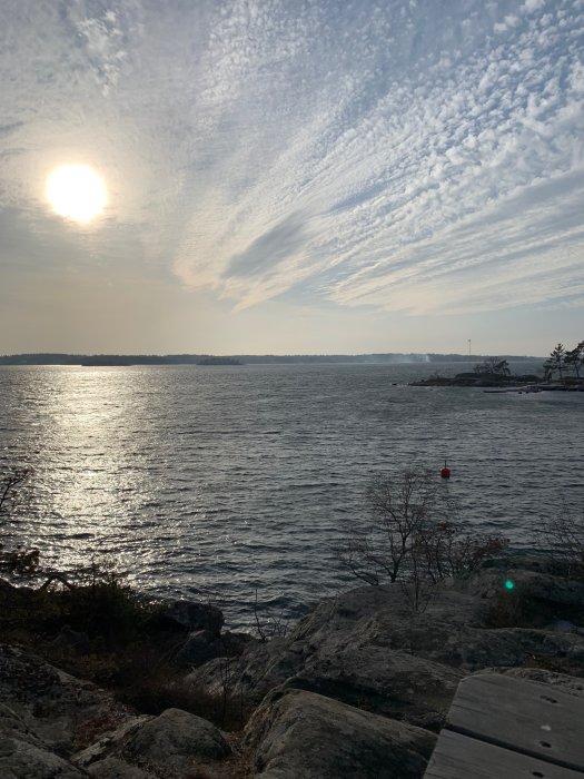 Solnedgång över havet med molnstrimmor på himlen och klippor i förgrunden.