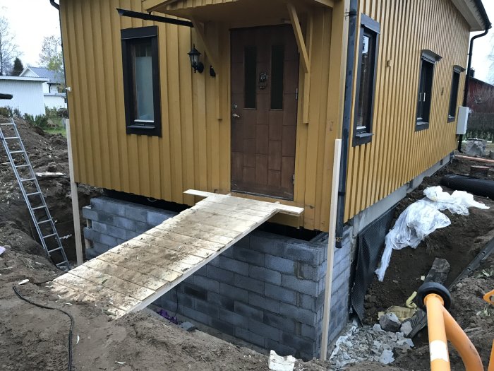 Nybyggd källarvägg och pågående dränering vid en gul husfasad med öppen gräv.