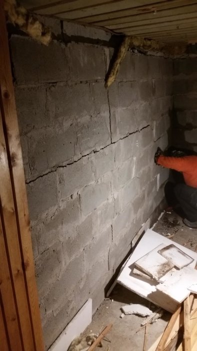 Person som avlägsnar panel från en fuktig och sprucken källarvägg.