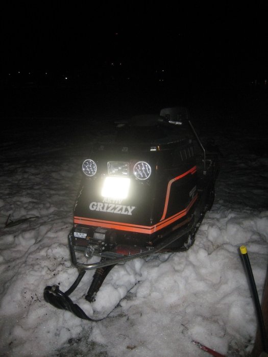 Snöskoter med monterad vinsch och LED-extraljus i snöig terräng under kvällstid.