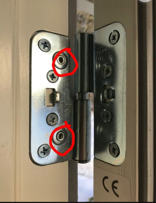 Dörr med närbild av justeringsskruvar på ett öppet gångjärn, markerade med rött för att visa justeringsmetoden.