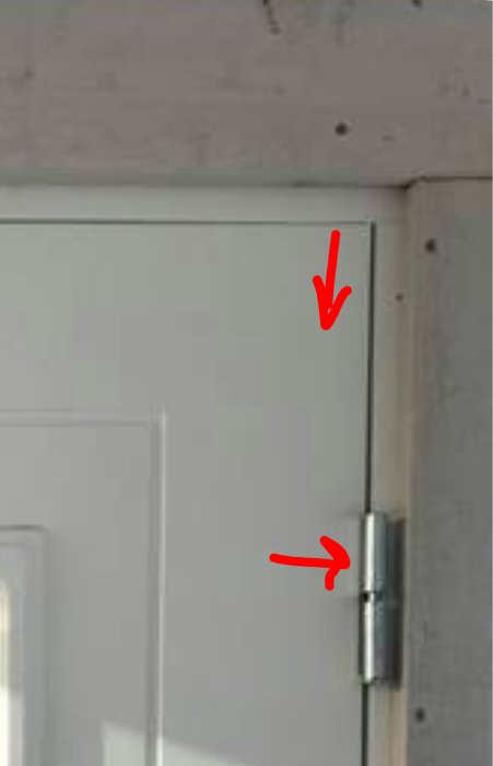 Gångjärn på en dörr med synlig springa upptill, markerad med en röd pil som pekar mot justeringsbehovet.