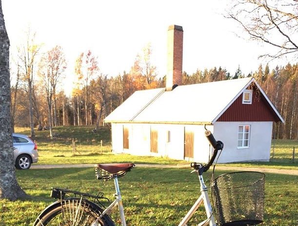 Ett rött gammalt pannhus med vit hög skorsten i lantlig miljö, en cykel i förgrunden.
