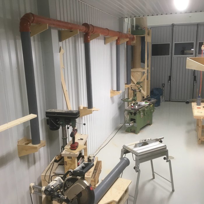 Verkstad med uppsatta rör och spjäll längs väggen, arbetsbänkar och verktygsmaskiner.