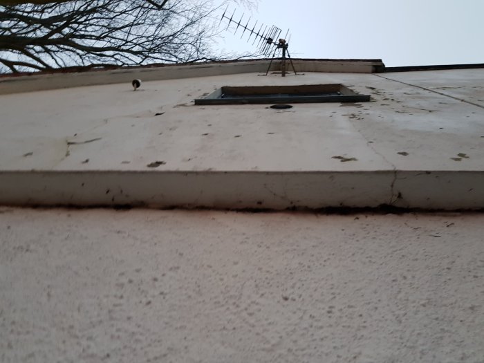 Fasad med sprickor och flagande puts, trolig tillbyggnad med synlig luftspalt.