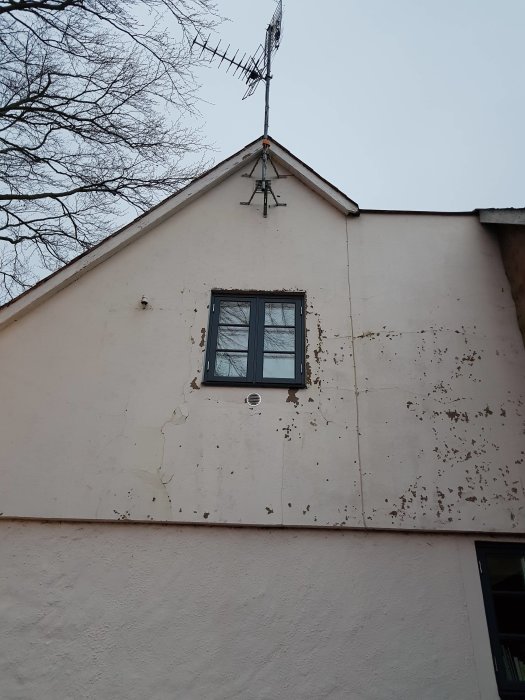 Husfasad med sprickor i putsen, avflagande färg och en antenn på taket.