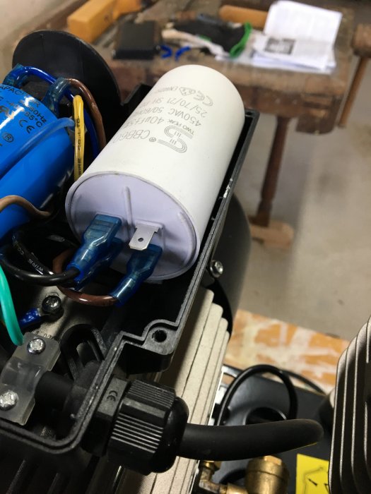 Elektriska komponenter och kondensator i ett uppplockat apparatskal på en arbetsbänk.