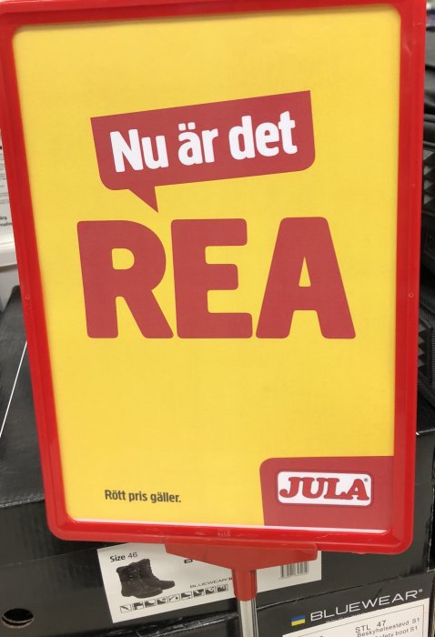 Rea-skylt från Jula med texten "Nu är det REA" och "Rött pris gäller" på en gul bakgrund.