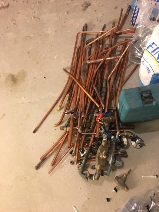 Utdragna kopparledningar och gamla VVS-komponenter på ett betonggolv, demonterade för renovering.