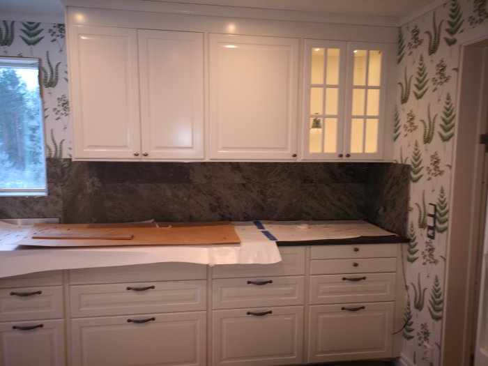 Köksskåp i off white med luckor och lådfronter, dekorativ sockel och marmorbänkskiva.