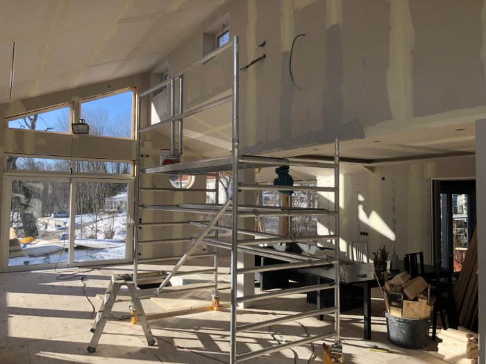 Inomhusbyggarbetsplats med gipstäckta väggar och tak, plywood, stegar och renoveringsutrustning under förberedelse för målning.