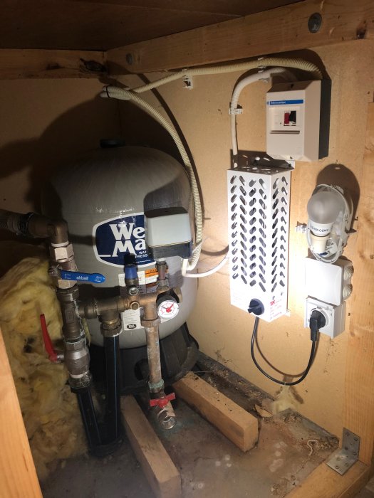 Hydropress och olika vattenpumpskomponenter i ett garage, med elektrisk låda och knappar.