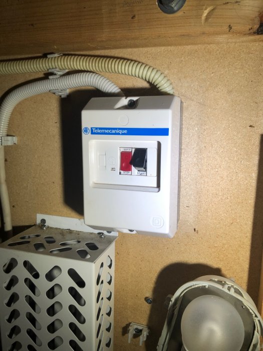 Motor-skyddsbrytare med röd stoppknapp och svart startknapp i ett garage, kopplad till en brunnsinstallation.