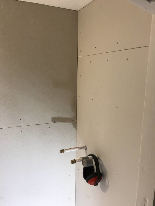 Gipsväggar i hörn av litet badrum med synliga VVS-installationer under renovering.