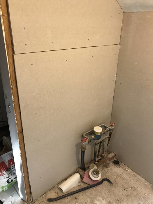 Rumsrenovering med nyinstallerade gipsskivor och synliga rörinstallationer i en hörna.