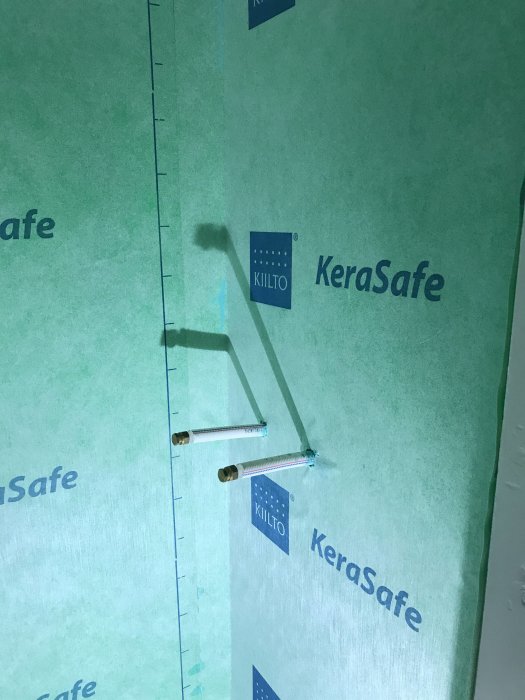 Vägg klädd i grönt fuktspärrmaterial med Kiilto KeraSafe logo, förberedd för installation av armatur.