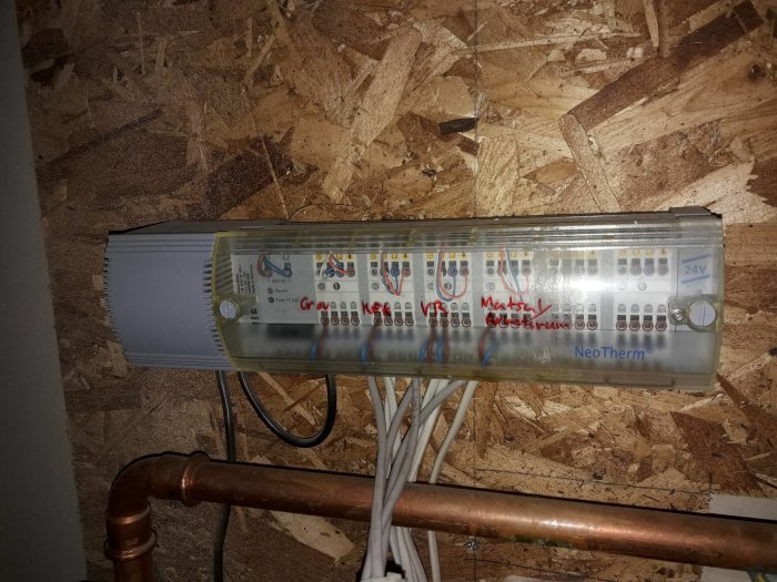 En golvvärmefördelare av märket Neotherm monterad på en OSB-skiva med synliga kopplingar och elektriska kablar.
