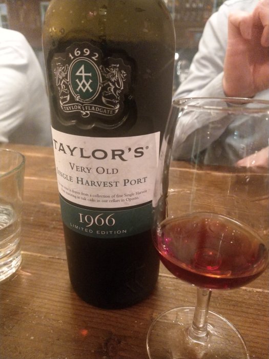 Flaska av Taylors Very Old Single Harvest Port 1966 och ett glas med mörkrött portvin, nära en ostbricka.