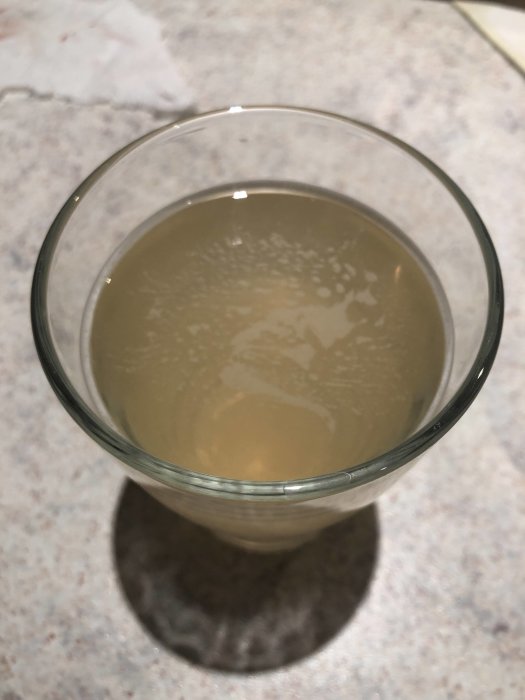 Ett glas med brunt och grumligt vatten står på en yta av marmor.