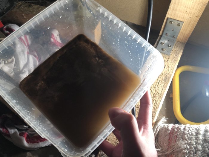 Hand som håller en plastbehållare fylld med brunt och grumligt vatten, tecken på järnbeläggning.