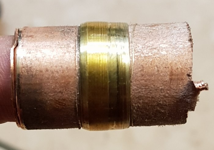 Närbild på en kopparledningskulvert med misslyckad klämringskoppling, som visar deformation av klämring och rör.