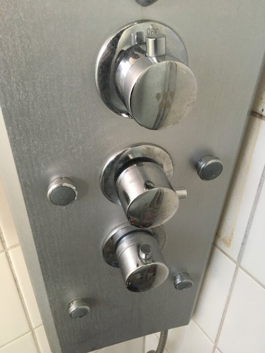 Duschreglage med tre knoppar på grå vägg, mellersta reglaget för vattenflöde.