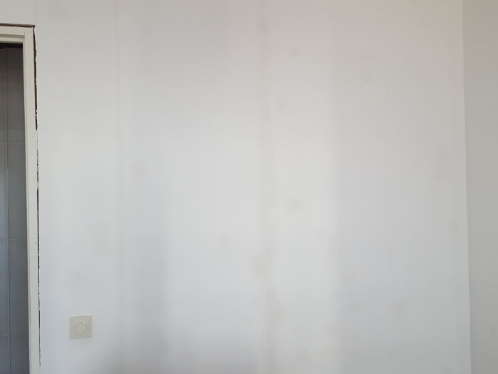 Vit vägg med synliga sprickor och lagningar med fog och spackel i ett sovrum.